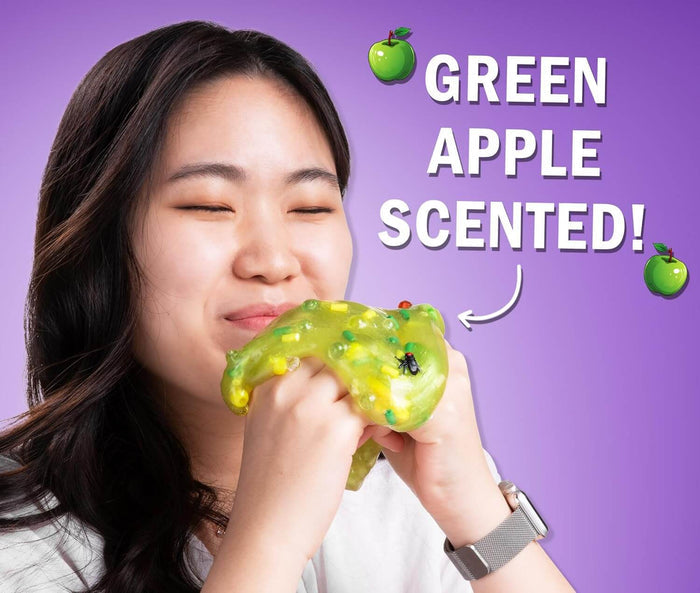 Woman smelling translucent green slime with fly and corn charms. Text: Green Apple Scented!