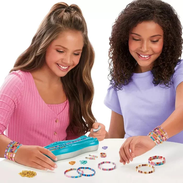 Two girls making colorful flat bead bracelets with a blue organizing case and scattered beads on a white table.