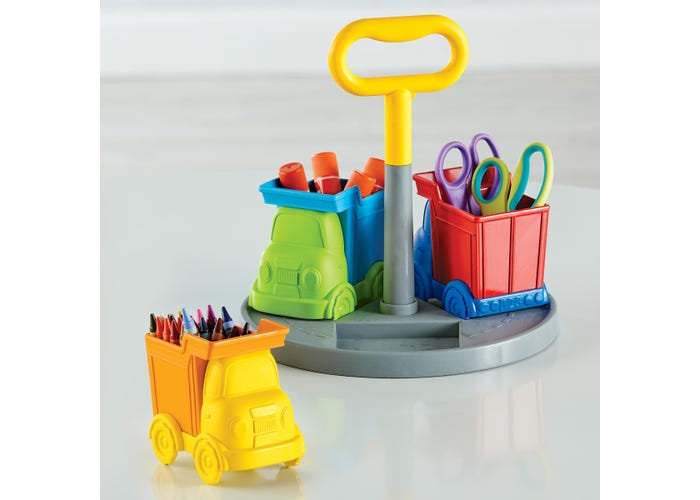 Colorful toy truck bins on a rotating gray base with a yellow handle, filled with crayons, scissors, and glue sticks.