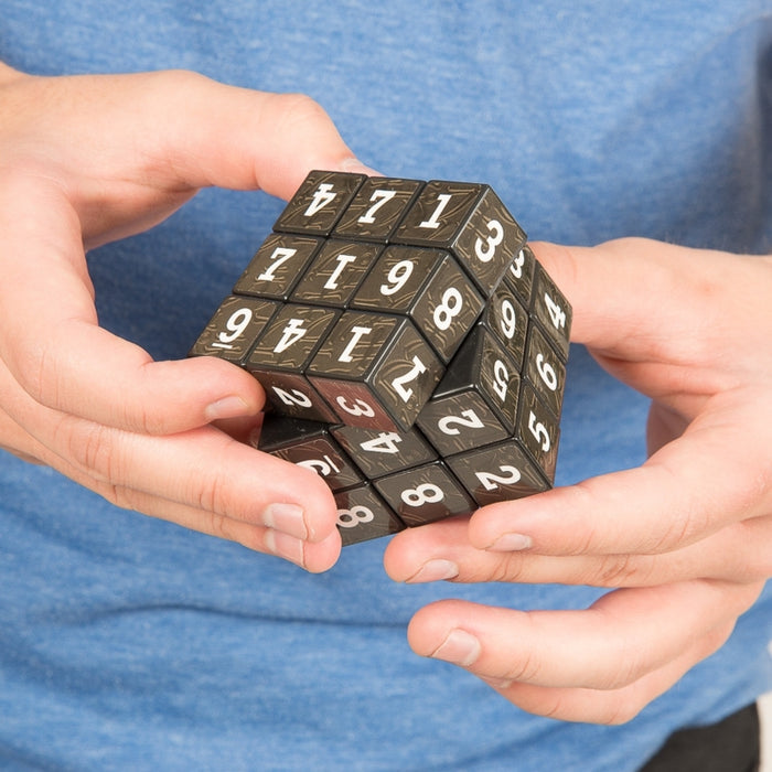 Hands holding a black 3x3 puzzle cube with white numbers 1-9 on each tile, shown partially rotated.
