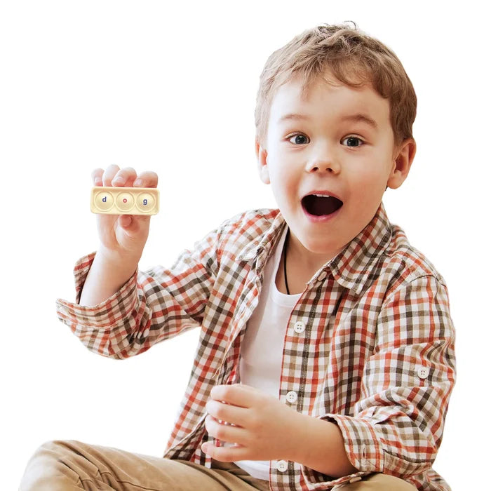 Excited boy in a plaid shirt holding a beige sensory board with three pop buttons spelling the word dog.