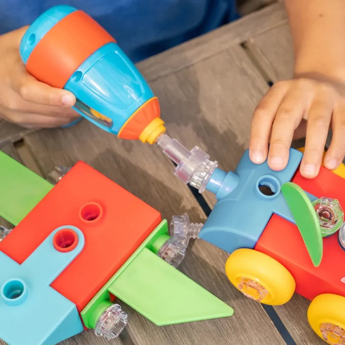 Child using a blue and orange toy drill to attach clear bolts to a colorful red, blue, and green toy airplane.