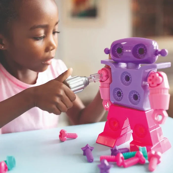A child uses a silver toy drill on a purple and pink robot with colorful plastic screws on a light blue table.
