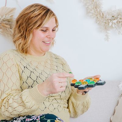 Woman in a yellow sweater placing colorful, translucent faceted gems onto a black cross-shaped board game.