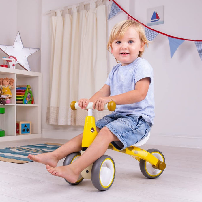 Toddler riding a yellow giraffe-themed ride-on toy with brown spots, mustard yellow handles, and grey wheels.