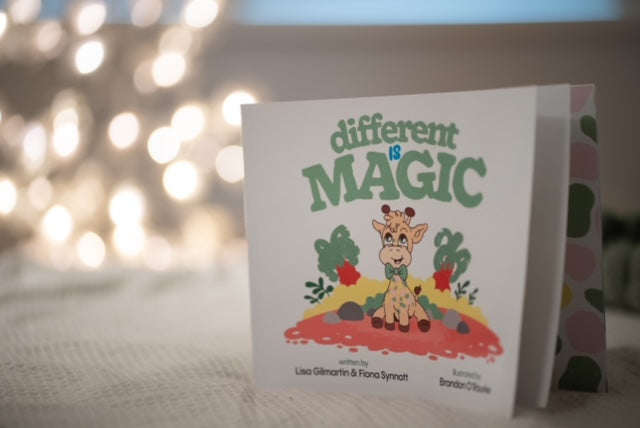 Square children's book titled Different is Magic with a cute giraffe illustration, set against warm, blurry lights.
