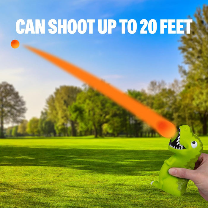 Hand squeezing a green T-Rex toy shooting an orange foam ball in a park. Text: CAN SHOOT UP TO 20 FEET.