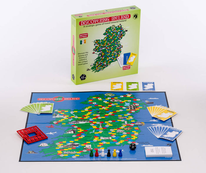 Green game box stands behind a blue board showing a colorful map of Ireland, card decks, pawns, and a black die.