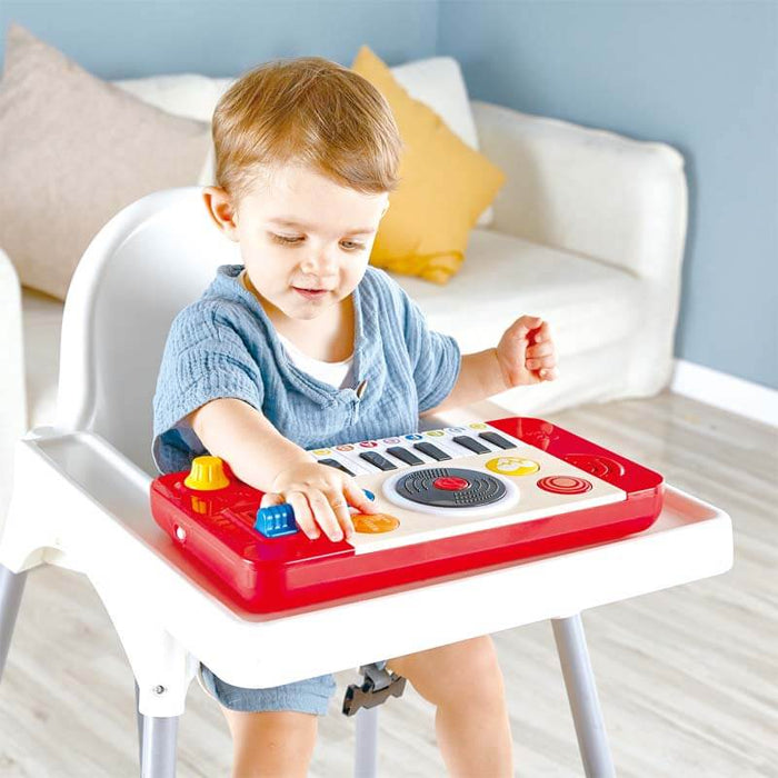 Toddler in a high chair plays with a red toy keyboard and spinning turntable featuring colorful buttons.
