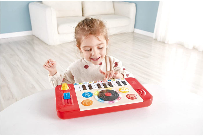 Young girl playing with a red and white musical toy featuring piano keys and a light-up spinning turntable.