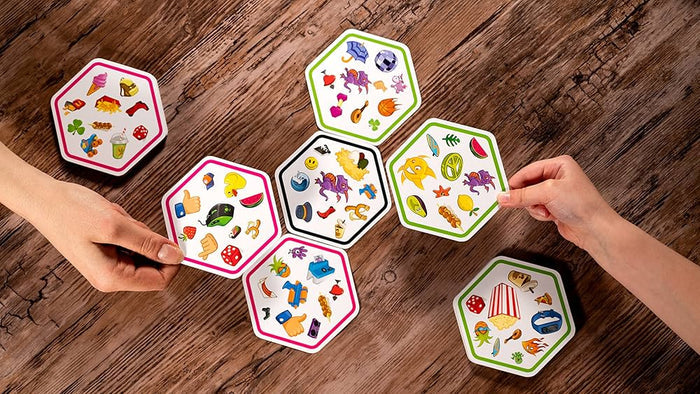 Hands placing hexagonal cards with colorful symbols onto a wooden table to connect matching icons.