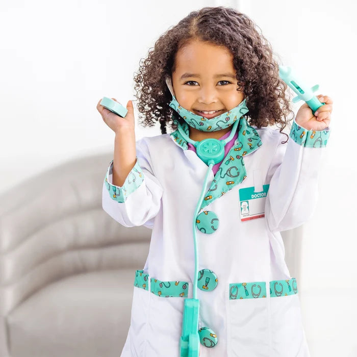 Girl in white doctor's coat with teal patterned trim, matching stethoscope, mask, and holding toy medical tools.