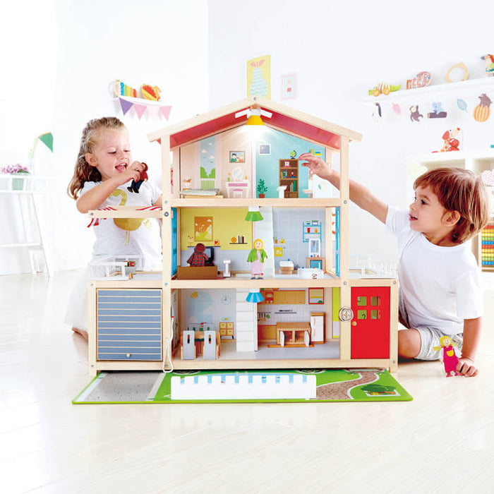 Wooden three-story dollhouse with red roof, working lights, and furniture, shown with two children playing.
