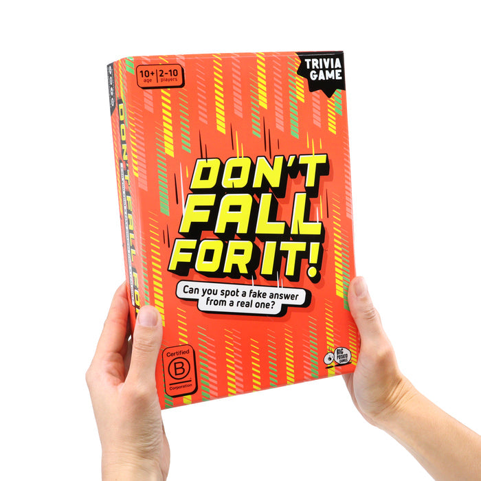 Hands holding an orange trivia game box with bold yellow text and diagonal green and yellow stripe patterns.