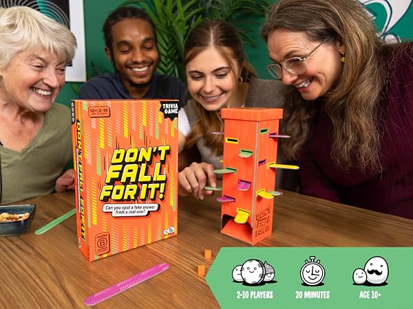 Four people play a trivia game with an orange box and a tower with colorful sticks on a wooden table.