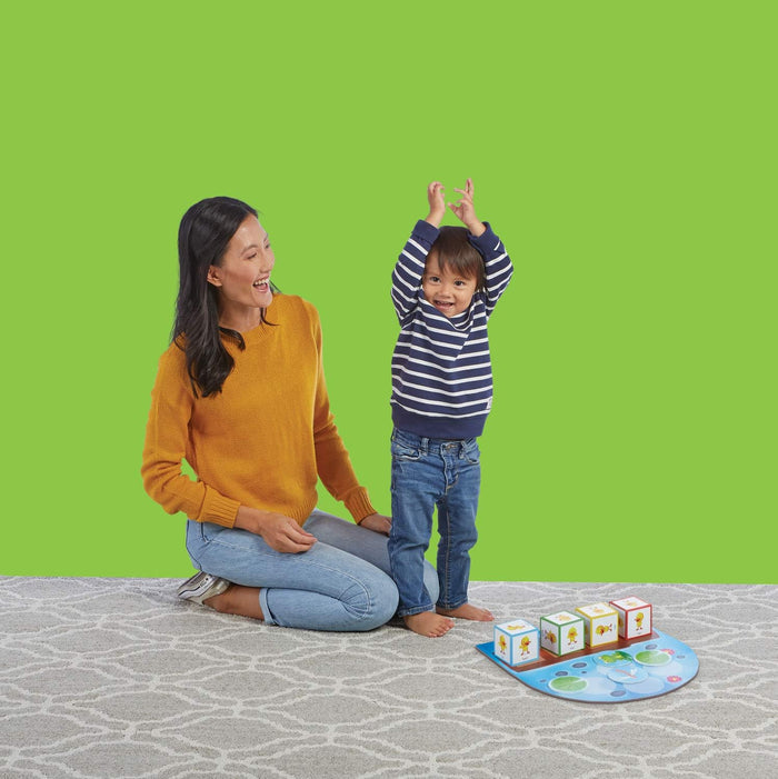 Woman and child play with colorful duck blocks and a lily pad game mat against a bright green background.