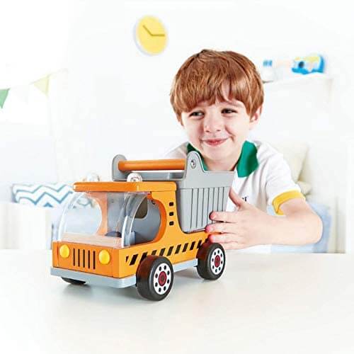 A young boy plays with a bright orange and grey wooden toy dumper truck featuring large black wheels.