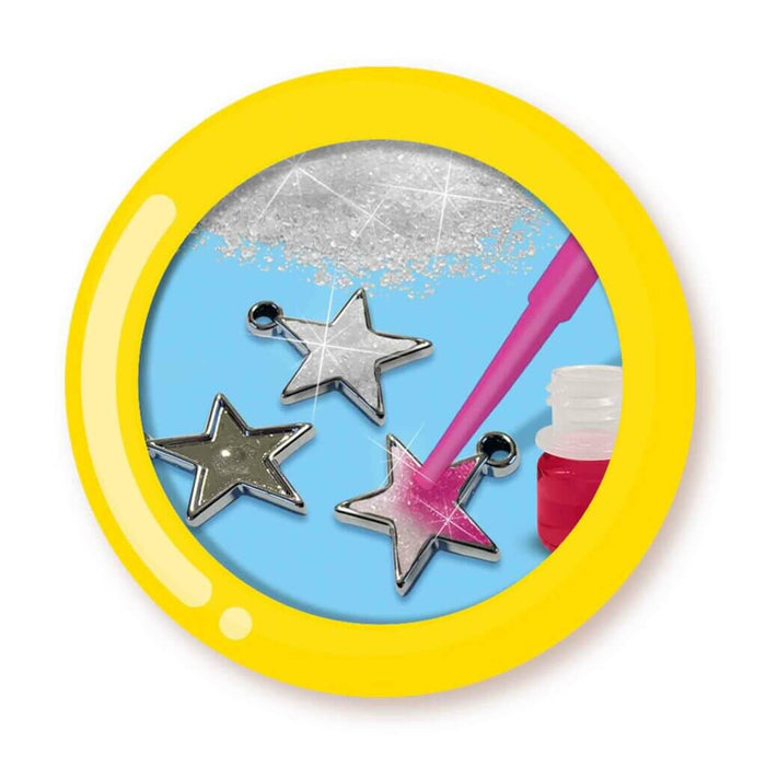 Star charms being decorated with pink liquid and silver glitter, shown inside a yellow circular frame.