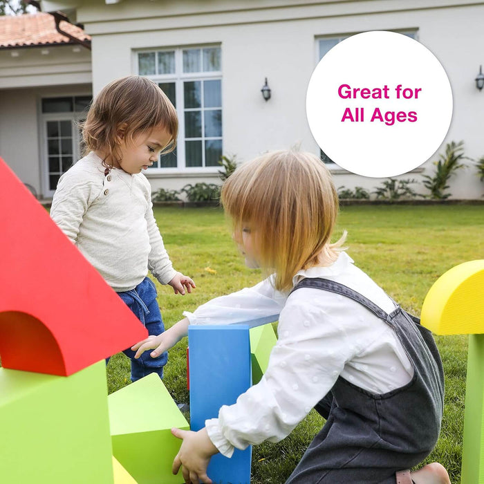 Two children playing with giant red, blue, and green foam building blocks on a green lawn.