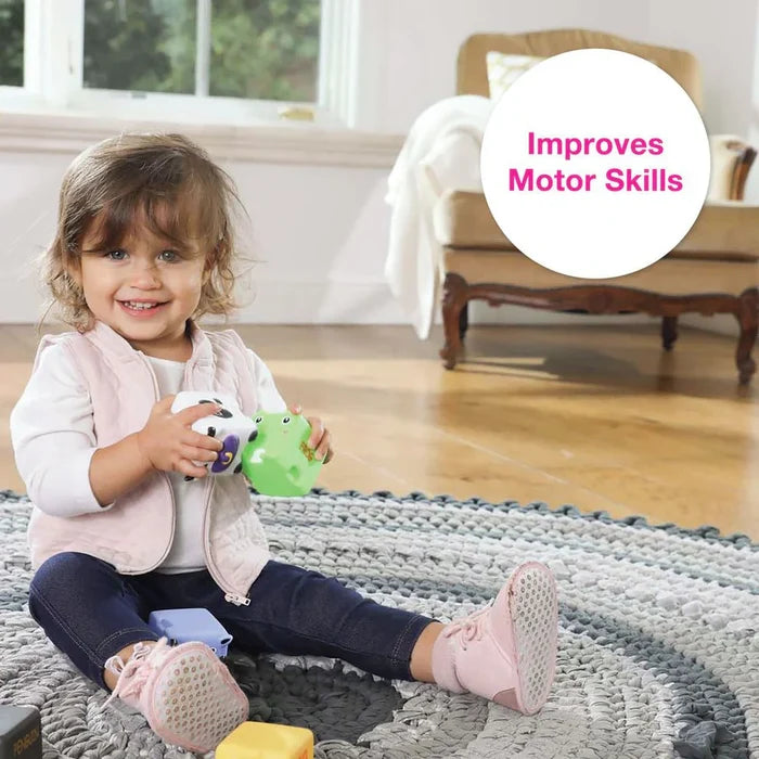 Smiling child holds soft green frog and white cow blocks. Text overlay says Improves Motor Skills.