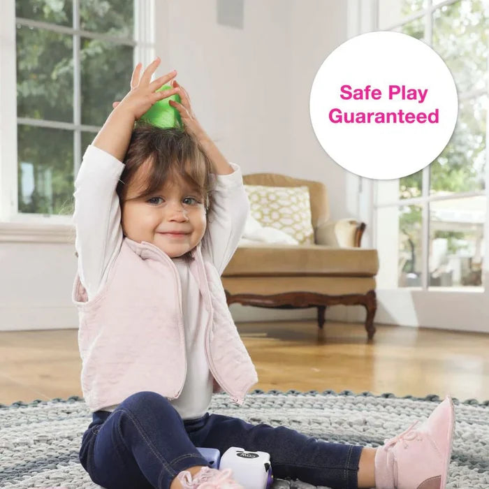 Toddler sits on a rug holding a green squeeze block above her head next to animal-themed soft blocks.
