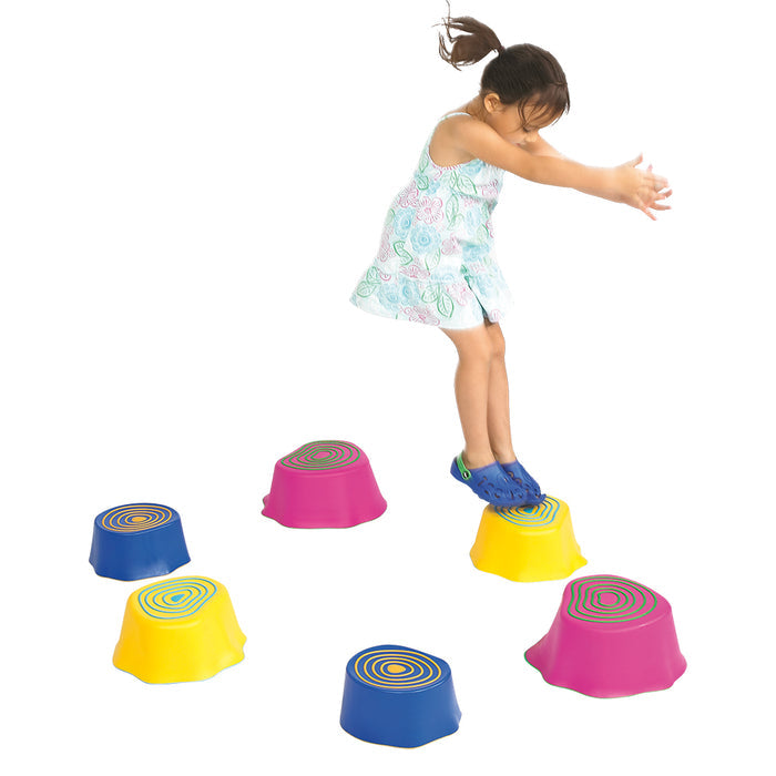 Young girl jumping on colorful stump-shaped stepping stones in pink, blue, and yellow with wood grain patterns.