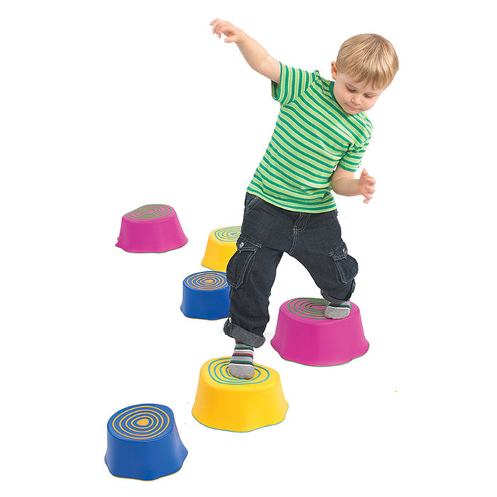 Boy balancing on colorful pink, yellow, and blue tree stump-shaped stepping stones with textured rings on top.