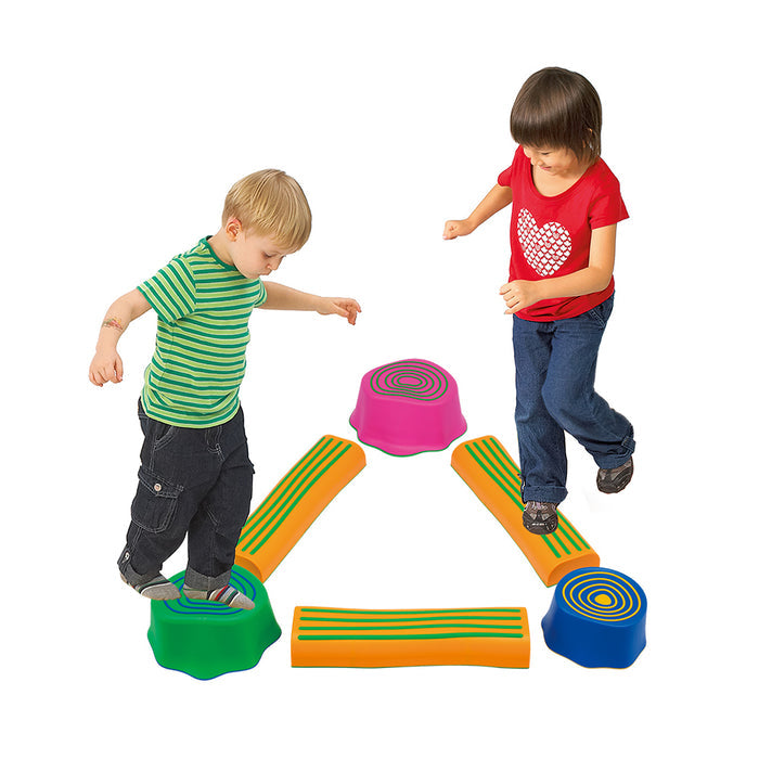 Two children balance on orange log beams and colorful pink, blue, and green stepping stone stumps.