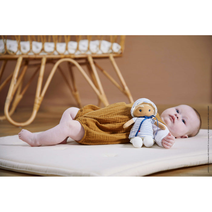 Soft plush doll with tan skin, blond hair, and a blue and white striped hoodie lying on a mat next to a baby.