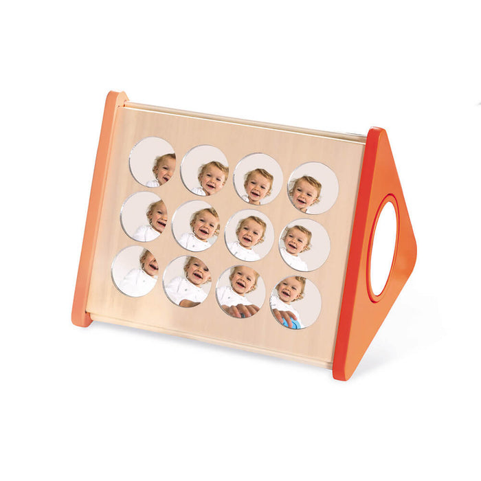 Triangular wooden mirror toy with orange side handles and twelve round mirrors reflecting a smiling baby.
