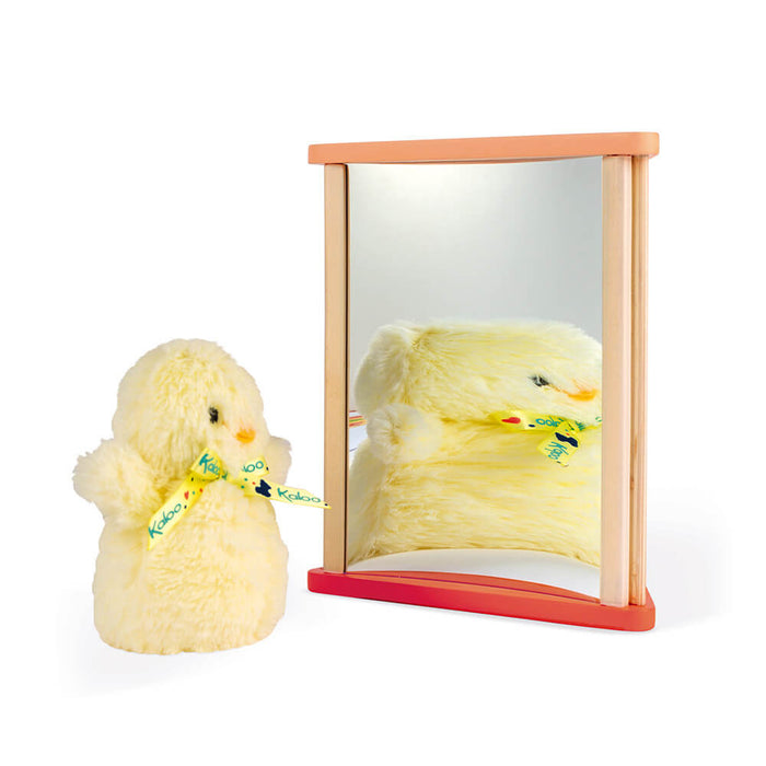 A small yellow plush chick reflected in a curved mirror set in a light wood frame on a red base.