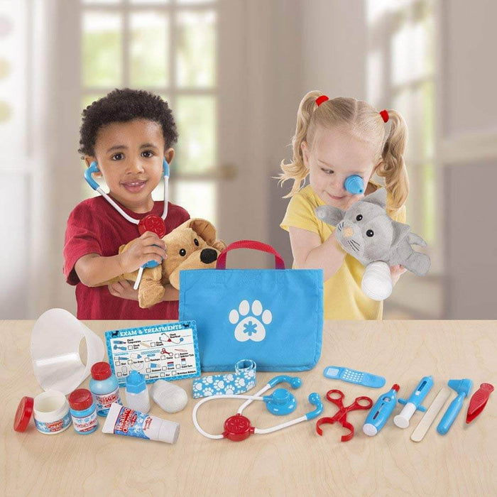 Two kids playing vet with stuffed animals, a blue paw-print bag, and various colorful toy medical tools on a table.