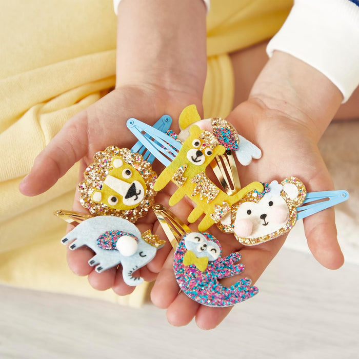 Child holding five colorful felt and glitter animal hair clips: a lion, tiger, monkey, sloth, and elephant.
