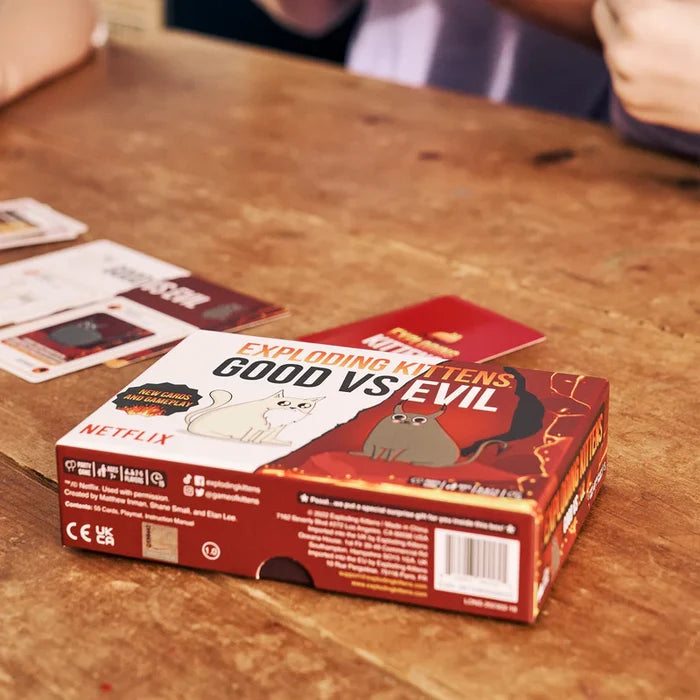 Rectangular game box featuring a white kitten and grey devil cat on a wooden table with scattered playing cards.