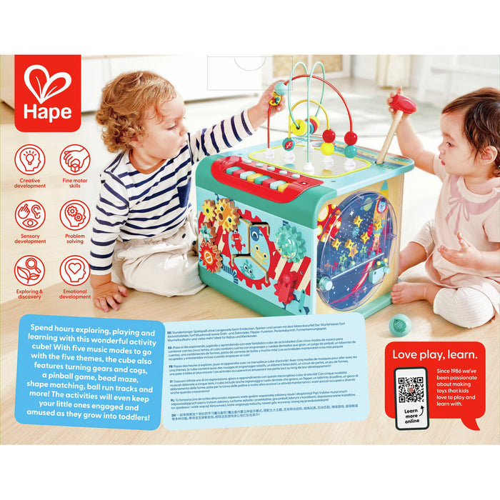 Two toddlers play with a teal wooden activity cube featuring a bead maze, colorful gears, and shape-matching slots.