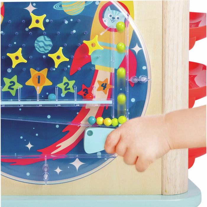 Child's hand operating a space-themed marble game on a wooden activity cube with colorful balls and stars.