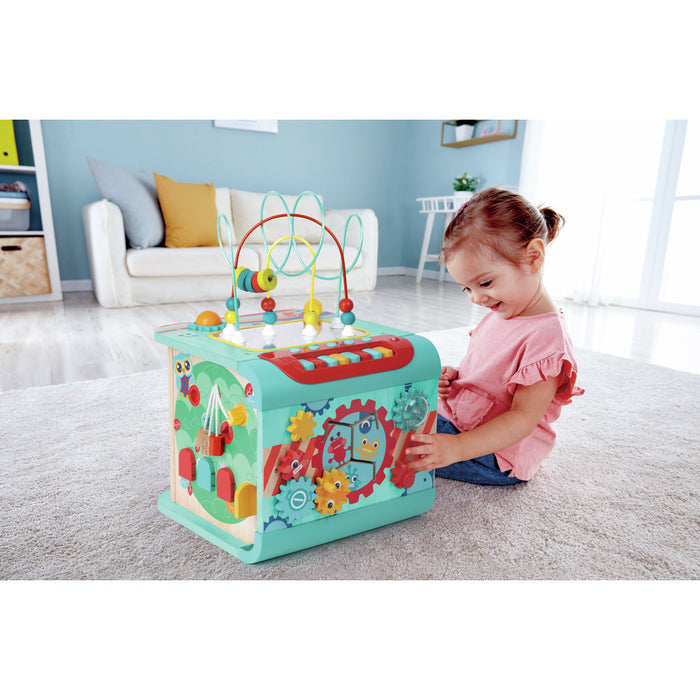 Young girl playing with a teal sensory activity cube featuring colorful gears, wire bead maze, and musical keys.