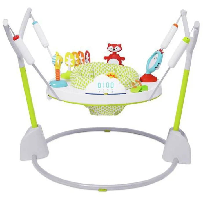 White and green baby activity jumper with a patterned fabric seat, toy-filled tray, and a circular gray floor base.