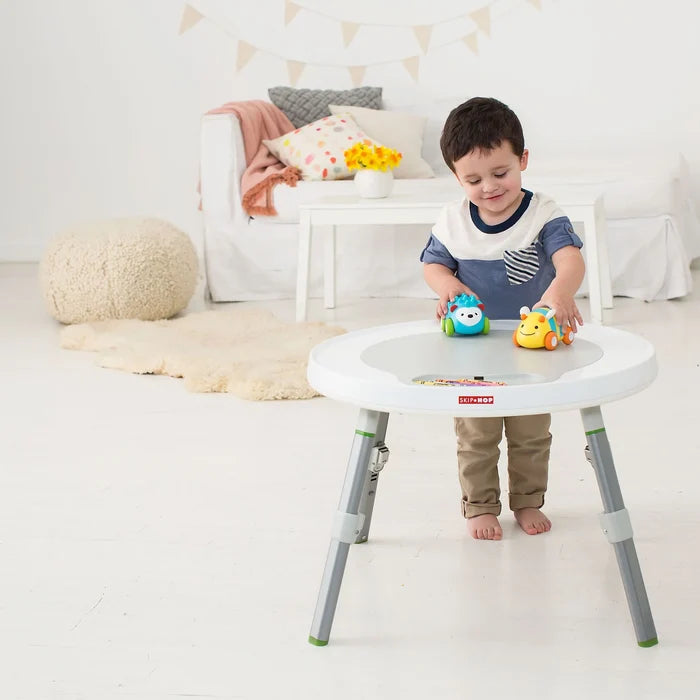 Toddler playing with toys on a round white activity table with grey legs and green accents.
