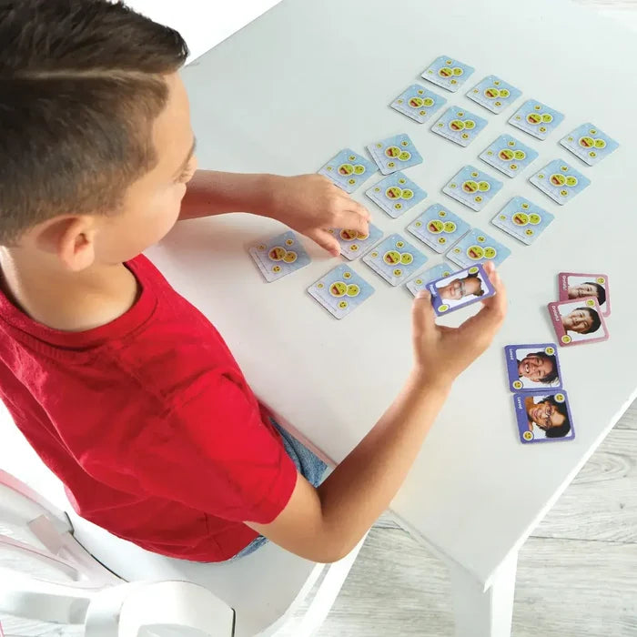 Child matching emoji-patterned cards with photos of diverse children expressing emotions on a white table.