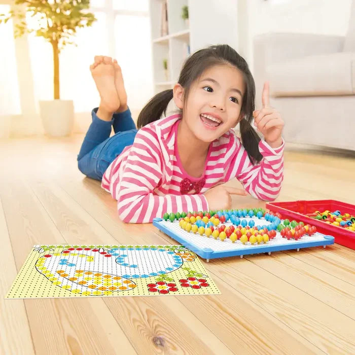A smiling girl uses colorful mushroom-shaped pegs on a white board to match a pattern guide on a wooden floor.
