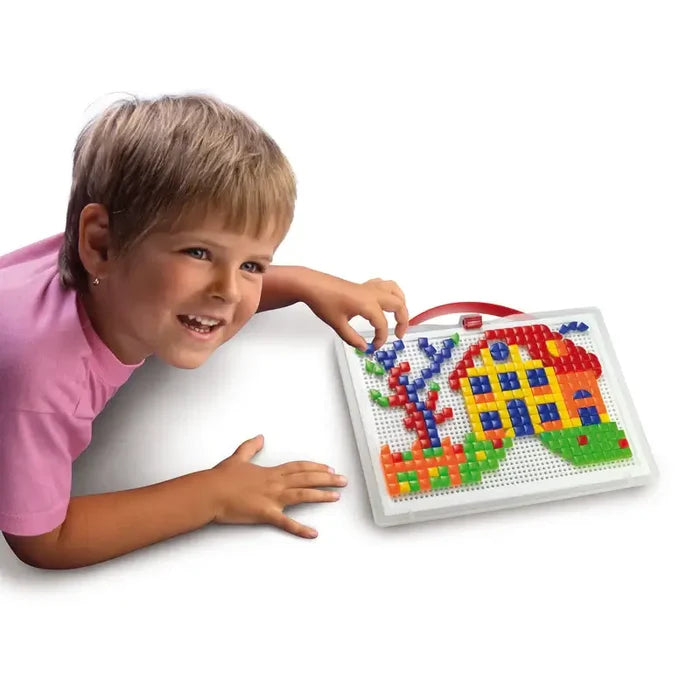 Smiling child builds a colorful house and tree mosaic using small plastic pegs on a portable white peg board.