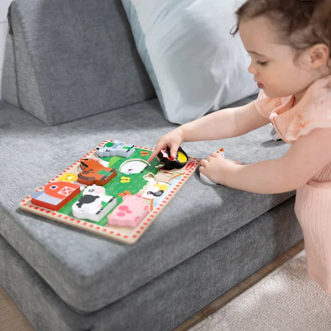 Toddler playing with an 8-piece chunky wooden farm animal puzzle on a grey fabric couch.