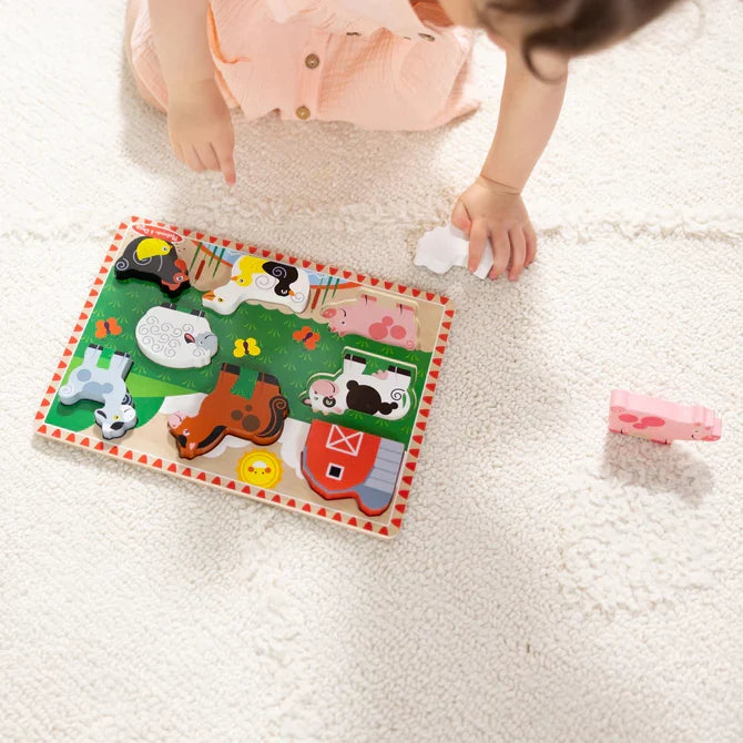 Toddler playing with a wooden farm animal chunky puzzle featuring a cow, pig, and barn on a white rug.