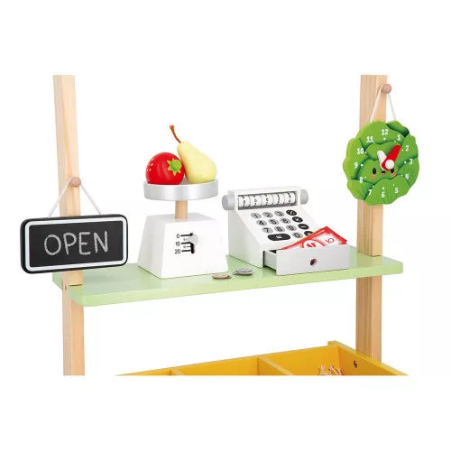 Wooden toy market with scale, play fruit, cash register, open sign, and vegetable clock on a light green shelf.