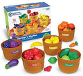 Five labeled brown toy baskets filled with colorful plastic fruits and vegetables next to their illustrated product box.