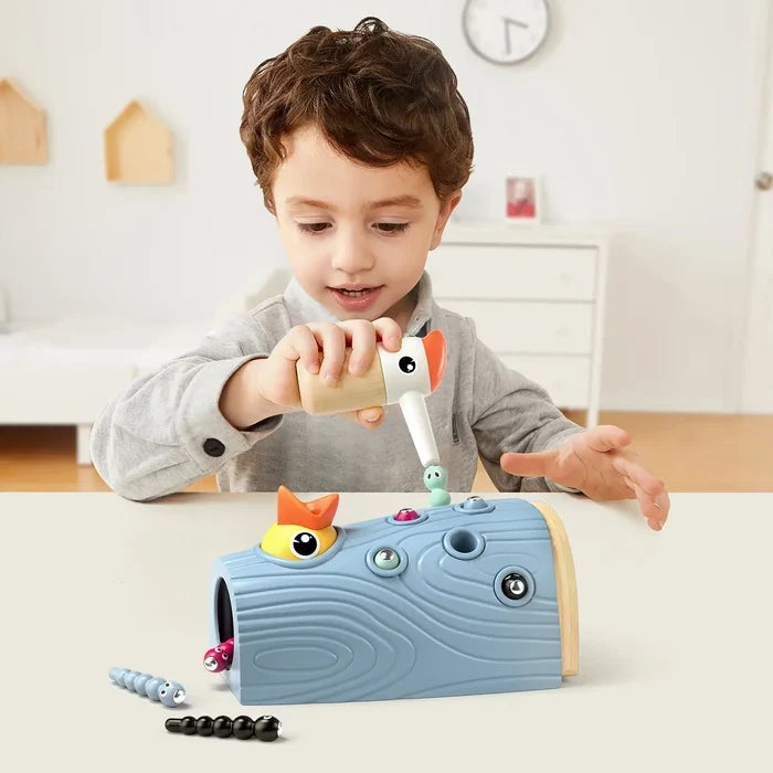 Child uses a magnetic woodpecker tool to pull colorful worms from a blue textured log to feed a baby yellow bird.