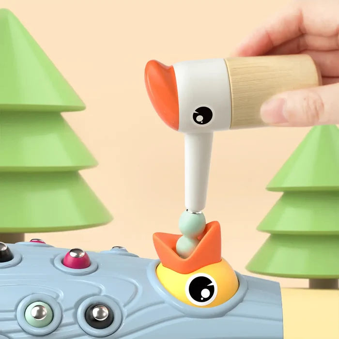 A hand uses a magnetic woodpecker toy to pull colorful worms from a blue log into a baby bird's open mouth.