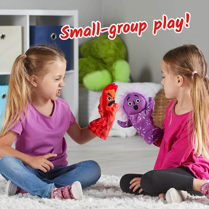 Two girls playing with a red angry hand puppet and a purple surprised hand puppet on a white rug.