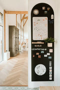 Tall arched black magnetic wallpaper on a white wall, decorated with educational magnets, numbers, and drawings.